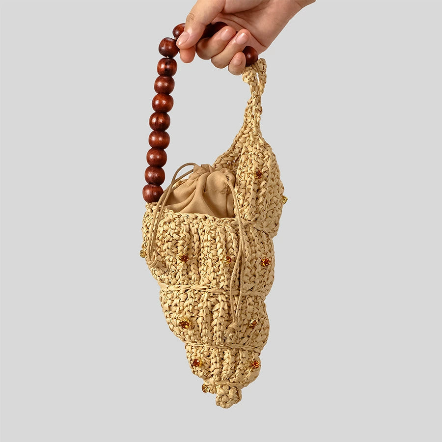 Shell-Shaped Straw. Featuring an artisanal woven straw shell design, a rustic wooden beaded handle—the perfect statement accessory for your next coastal getaway
