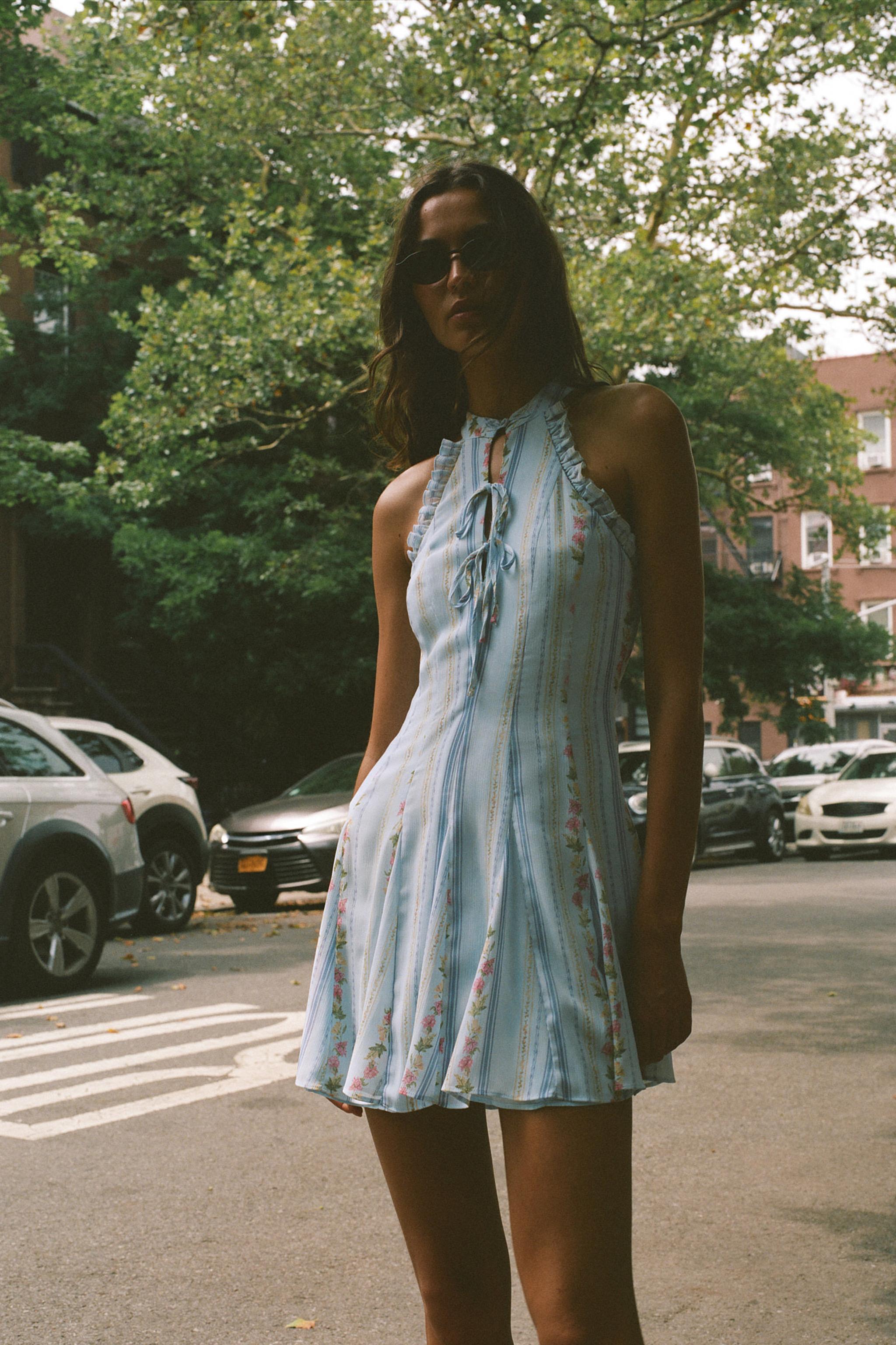 Featuring charming pink rose prints, a chic halter neckline with ruffle trim, this mini is the ultimate statement piece for sun-drenched coastal getaways.