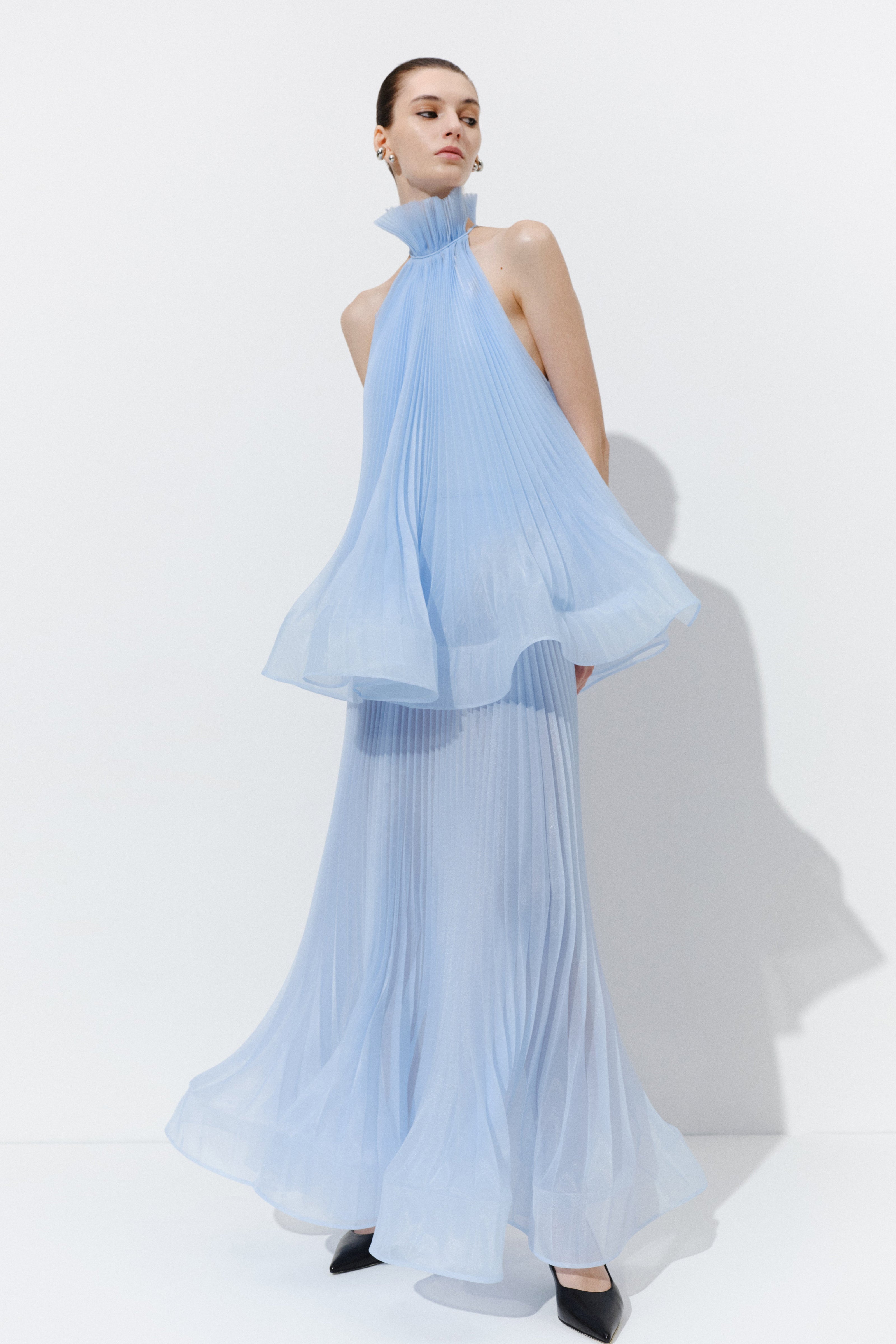 Featuring an blue pleated fabric, a high ruffled halter neckline, and a fluid matching maxi skirt, this set is the ultimate choice for luxury resort getaways.