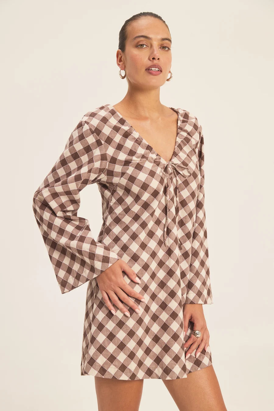 Featuring a timeless gingham check pattern,a delicate front tie closure, long flared sleeves, this dress is the ultimate statement piece for casual resort getaways.