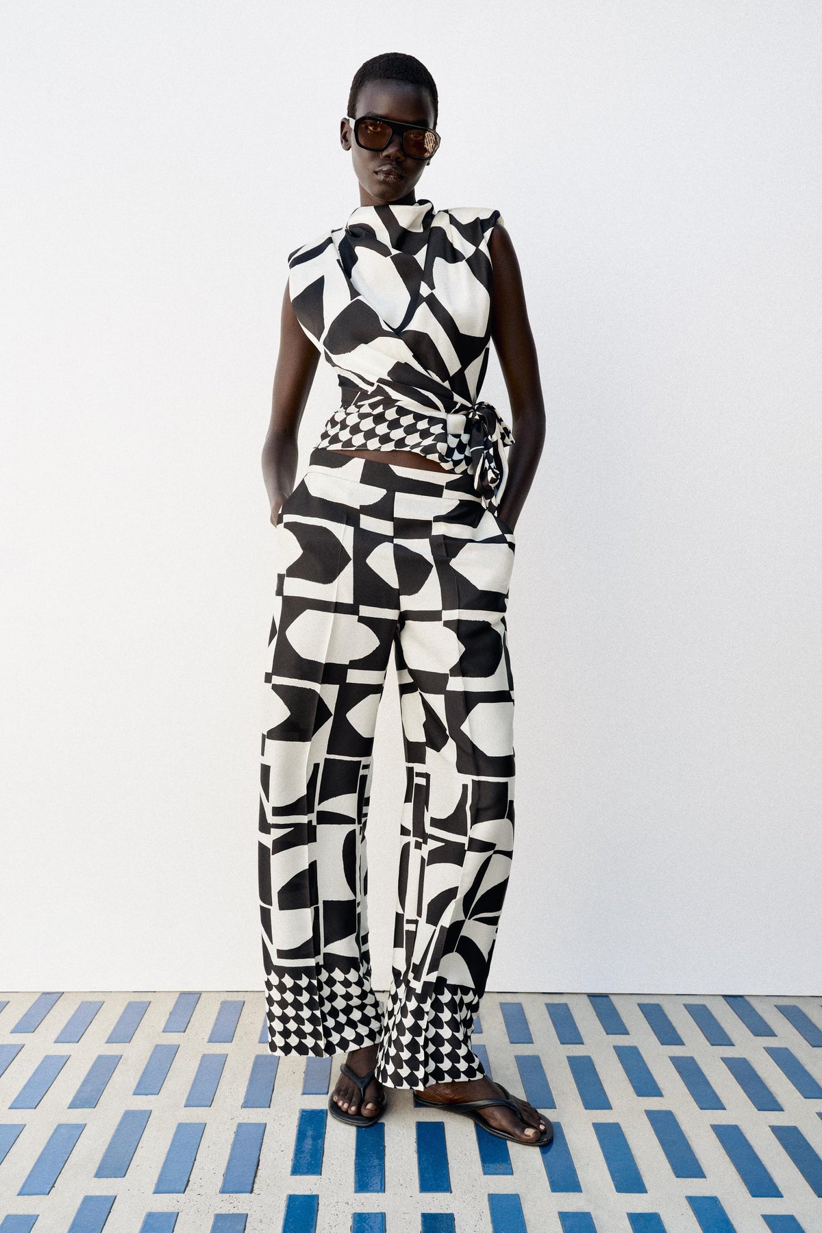 Featuring a bold black and white abstract graphic print, a sophisticated draped wrap top. this top is the ultimate statement piece for luxury resort getaways.